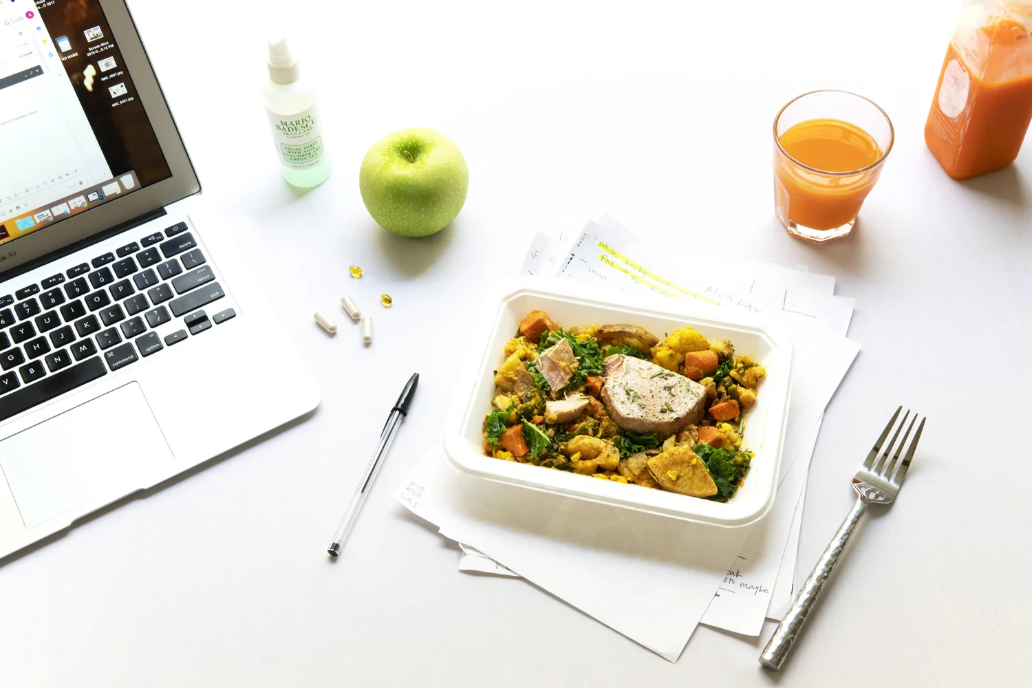 Healthy lunch at a desk: laptop, takeout bowl with rice and vegetables, apple, and juice